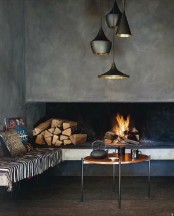a stylish and cozy fireplace nook with an open minimalist fireplace, some firewood and a bench with pillows plus a cluster of pendant lamps