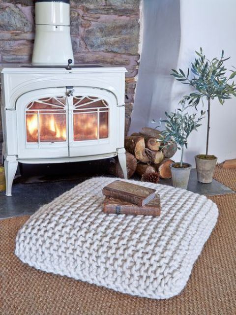 a white fireplace with firewood, potted plants, a crochet cushion is a lovely nook to spend time in