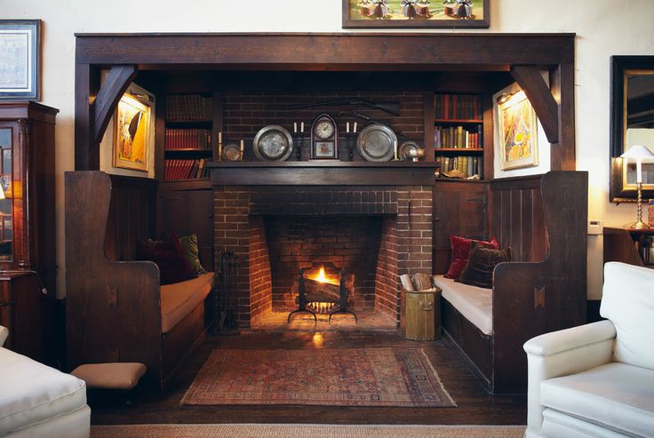 a dark and welcoming nook with a brick fireplace, a dark mantel with decor and tall benches with cushions and pillows