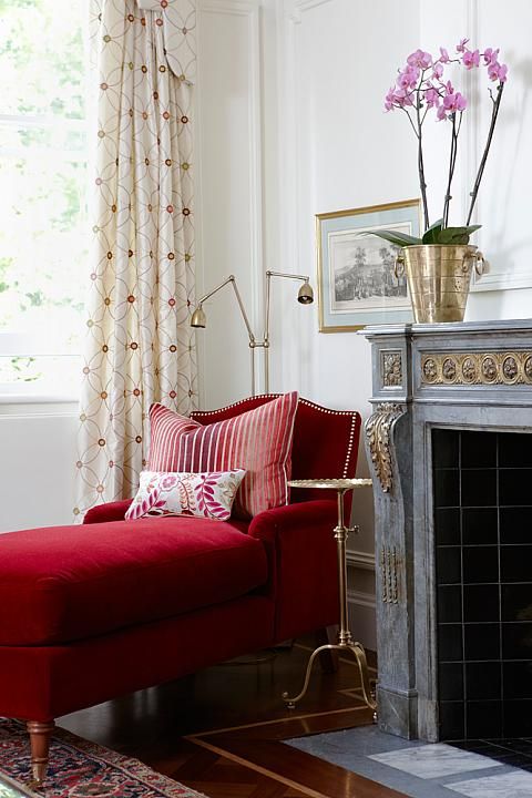 a fireplace nook with a refined and chic fireplace, a deep red lounger and a floor lamp plus a small round table between these two items for more elegance