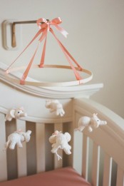 a cute nursery mobile with crochet white elephants and a pink ribbon on top is a cool and lovely solution for any kids’ space