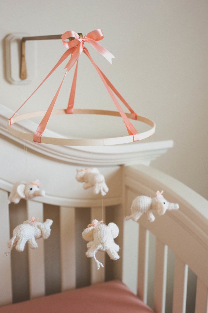 a cute nursery mobile with crochet white elephants and a pink ribbon on top is a cool and lovely solution for any kids' space