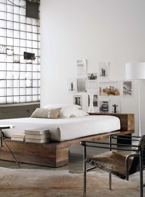 a neutral laconic bedroom done with industrial touches, with a stained wooden bed, a glass accent wall and a vintage metal and leather chair