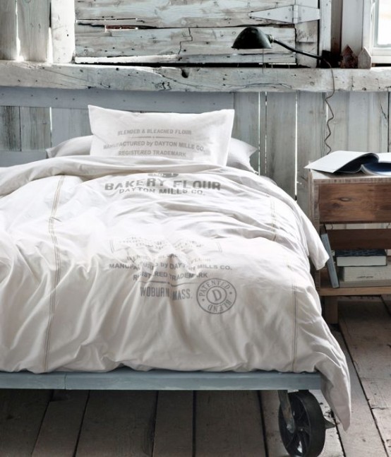 a whitewashed bedroom clad with wood, a metal bed on wheels, a wooden nightstand and a black table lamp is a lovely space to sleep in