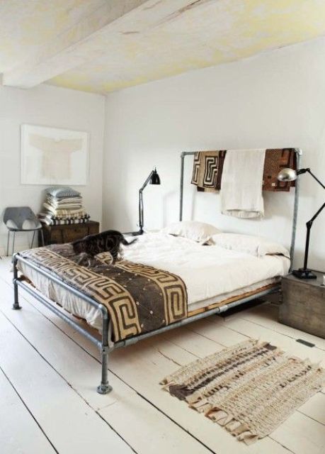 a neutral bedroom with an industrial bed made of metal and pipes, vintage wooden chests for storage and metal table lamps, printed textiles