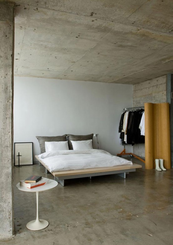 a minimalist meets industrial bedroom with concrete walls, ceiling and floors and ultra-minimalist furniture