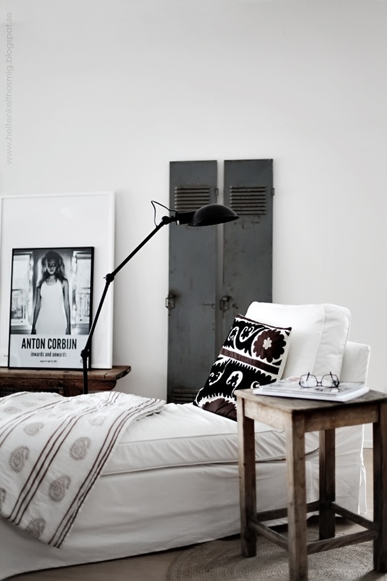 a neutral bedroom with industrial touches, with a metal file cabinet, a bed with white bedding, a wooden nightstand, a black industrial lamp and an artwork