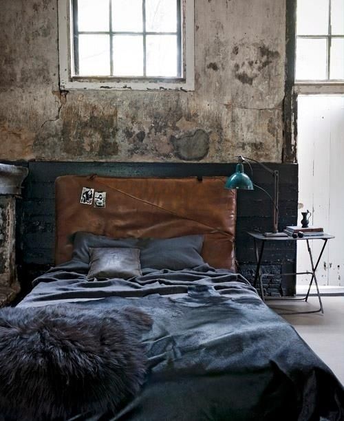 an industrial bedroom with shabby chic and rough walls, a bed with a leather headboard, a black metal nightstand and a vintage table lamp