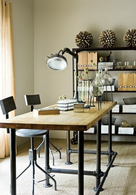 an industrial home office with a wood and metal double desk and tall stools, a large metal shelving unit, a large black metal table lamp