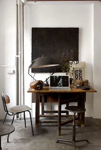 a small industrial home office with a vintage wooden desk, metal and wood chairs and stools, a large metal table lamp and a chalkboard