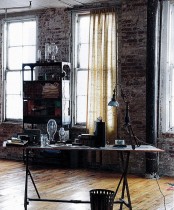 an industrial home office with whitewashed brick walls, a wood and metal desk, a metal shelving unit and a vintage table lamp