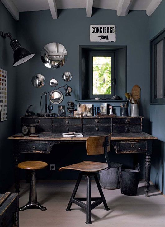a slate blue home office with a vintage black desk with a shabby touch, metal and wooden chairs, a gallery wall of round mirrors, black table lamps