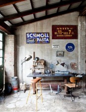 a shabby industrial home office with concrete walls with shabby brick walls, a metal desk and mismatching chairs, lots of vintage signs and a corrugated steel roof