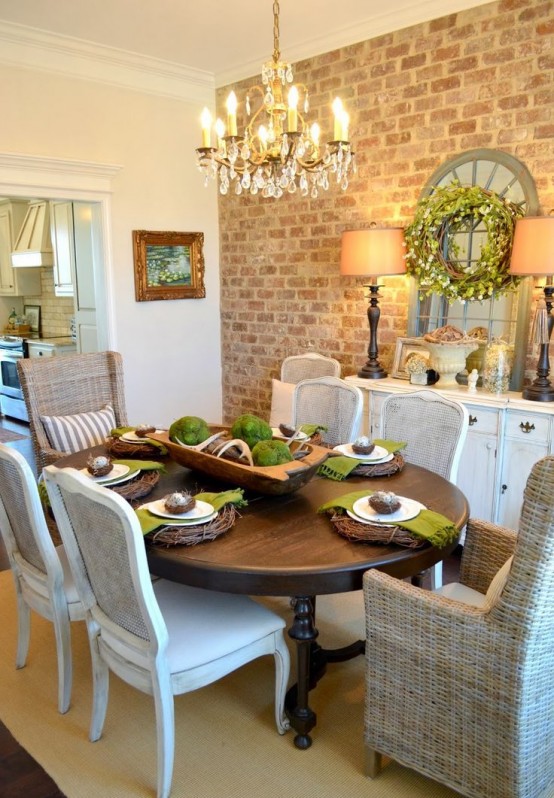 a vintage rustic dining space with an exposed brick accent wall, a vintage white sideboard, a dark-stained dining table, chic upholstered and wicker chairs in neutrals and a vintage crystal chandelier