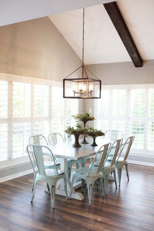 a vintage rustic dining space with a white dining table, white metal chairs, greenery and a metal frame pendant lamp