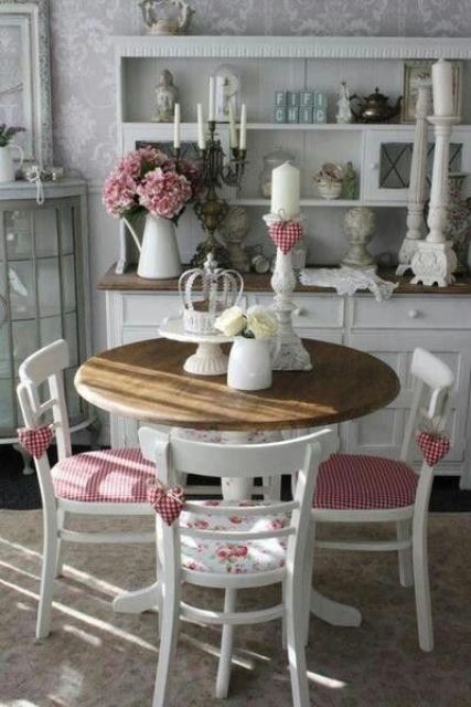 a vintage dining zone with a white buffet, white candleholders with pillar candles, a round table with a stained tabletop, white chairs with plaid upholstery is cute and lovely