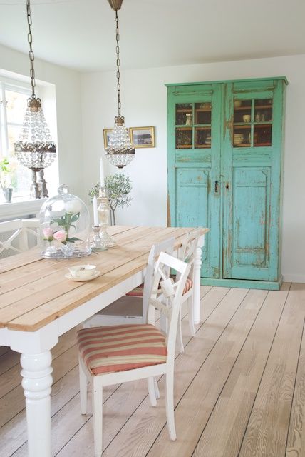 a vintage dining space with a green shabby chic cabinet, a white table with a stained tabletop, white chairs with upholstery and crystal chandeliers