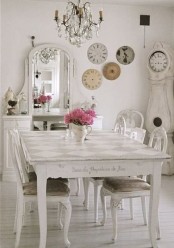 a refined neutral vintage dining zone with a shabby dinign table and matching chairs, a buffet with a mirror, a crystal chandelier and a gallery wall of vintage clocks