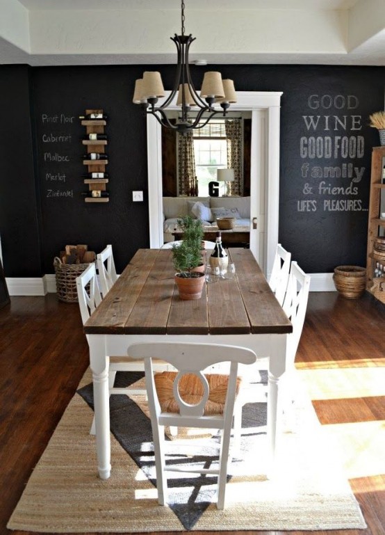 a vintage rustic dining space with chalkboard walls, a dining table with a stained tabletop, white chairs and a vintage chandelier over the table