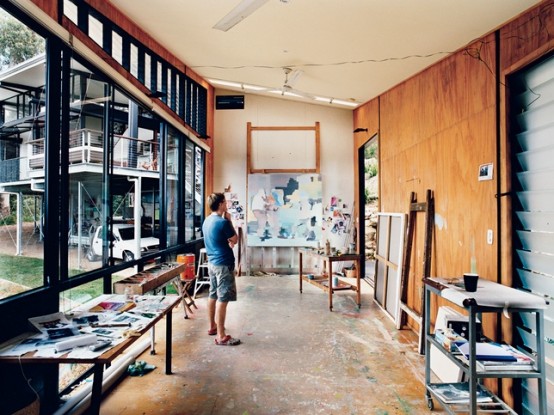 a large modern home artist studio with a glazed wall, several desks and stands, some artwork is a cool and light-filled space for creating