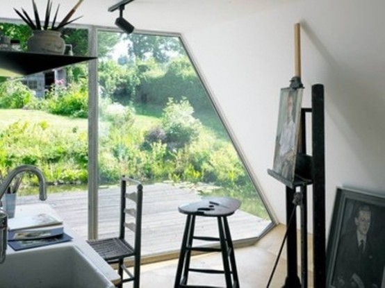 a small and cool modern artist studio in a garden pod, with a glazed wall, a desk, several stools, an easel and potted greenery