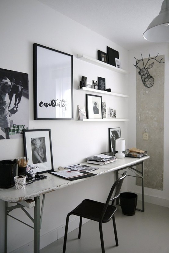 a modern black and white home artist studio with a sleek narrow desk, a black chair, ledges with wall art and some more black and white wall art