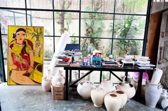 a light-filled home artist studio with a glazed wall, a large desk, pottery with paper and a large artwork is a cool space
