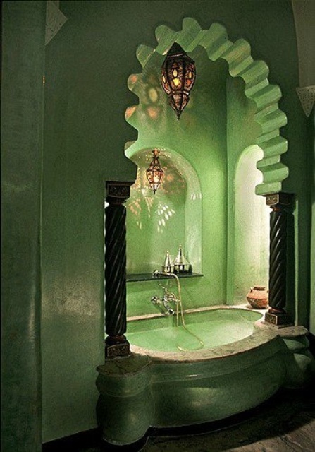 a grene Moroccan bathroom with a stone clad bathtub with pillars and a carved archway plus Moroccan lanterns