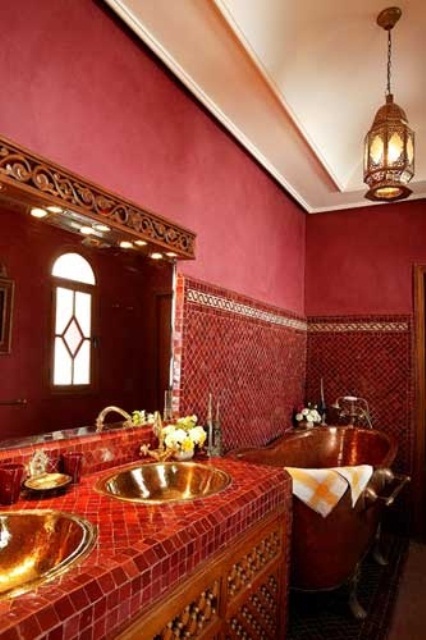 a burgundy bathroom done with plaster and tiles, with a tiled vanity, a pendant lamp and a wooden carved mirror frame