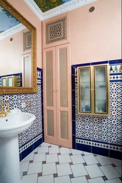 a pink bathroom with navy and white patterned tiles on the walls and floor, with a gilded frame mirror and a brass faucet