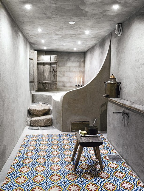 a contemporary Moroccan bathroom of concrete and with patterned tiles on the walls and floor, with a simple wooden stool and steps
