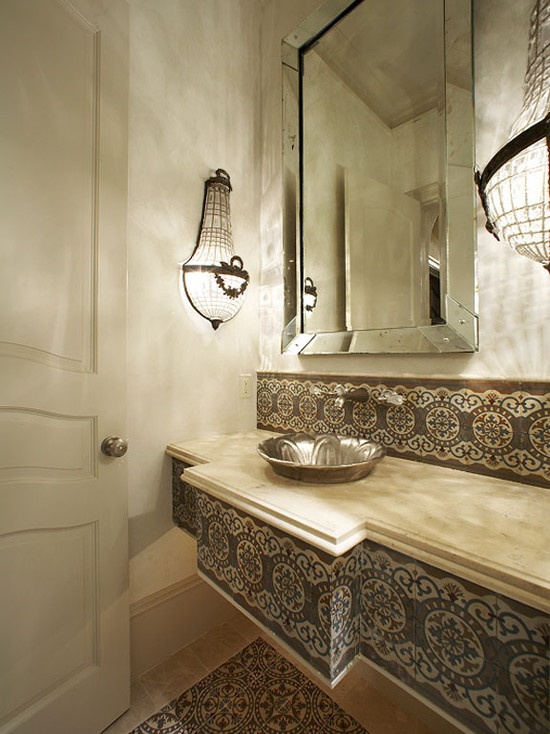 a neutral bathroom with patterned tiles that clad the vanity and wall, with catchy wall lamps