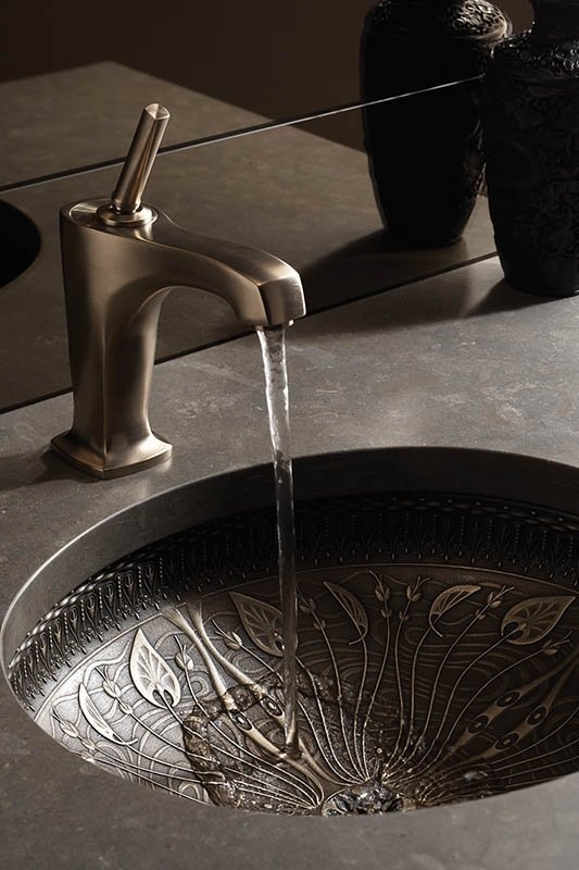 a stone vanity with a metal decorated sink and a matte faucet