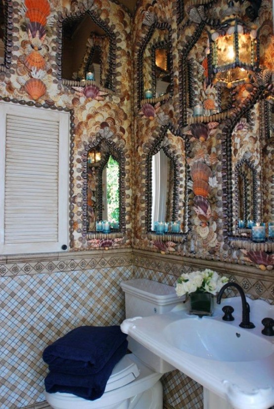 a catchy beach bathroom with sea shell clad walls, ornated mirrors, tiles and a shutter for decor