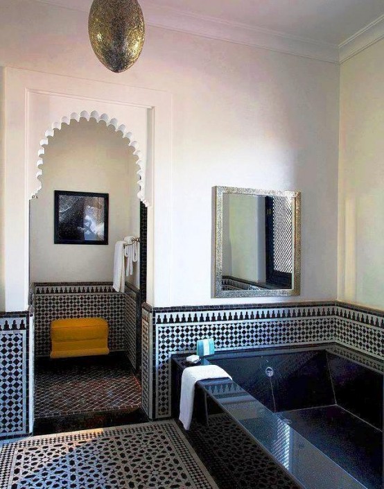 a navy and white bathroom with plaster and tile walls and floor, a tiled bathtub and a pendant lamp