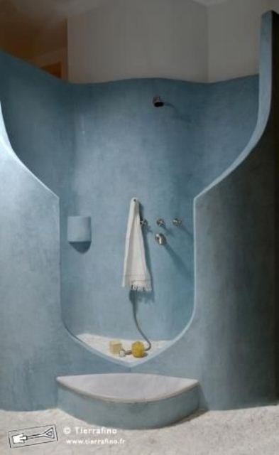 a blue plaster bathroom with a carved shower space and a concrete floor