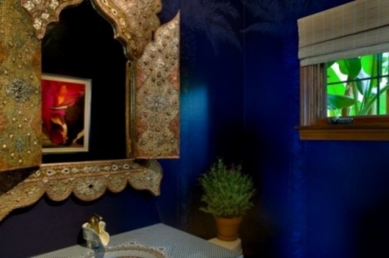 a bright blue bathroom with an ornated mirror, potted greenery and Roman shades