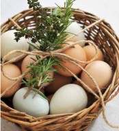a simple and cute rustic Easter decoration of a basket with naturally colored and pastel eggs, twine and greenery is a cool idea for a mantel or console table