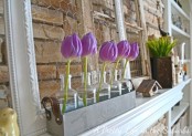 a purple tulip arrangement in bottles and some potted greenery for a cool spring mantel