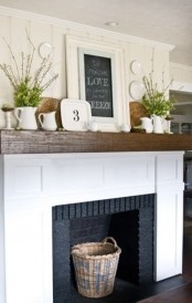 a rustic farmhouse mantel with blooming branches in jugs, decorative plates and a chalkboard