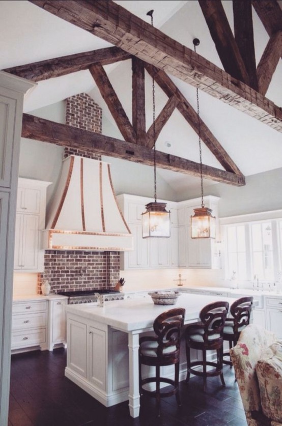 a refined white kitchen with chic cabinetry, a large metal hood, a brick backsplash, dark wooden beams with whimsy lantern hanging is very stylish