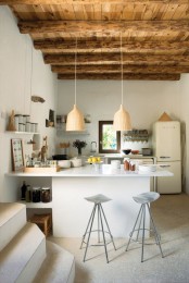 a modern white kitchen with an oversized white kitchen island, a wooden ceiling with beams for a warm and cozy feel and pendant woven lamps