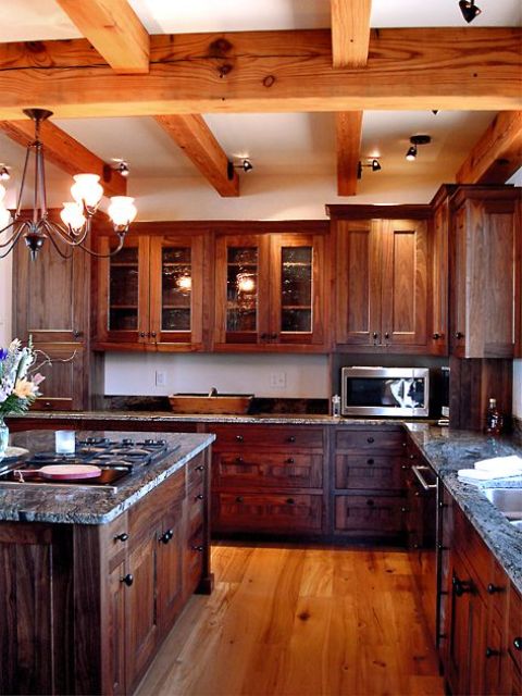 a dark farmhouse kitchen with wooden cabinetry and a kitchen island, wooden beams on the ceiling and matching wooden floors for a warm cozy feel