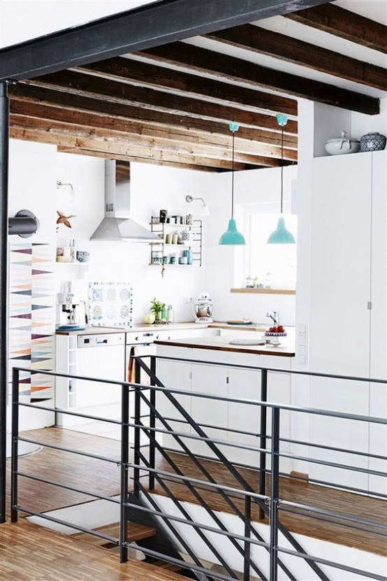 a minimalist white kitchen with sleek cabinetry, wooden countertops, wooden beams for a warm touch and blue pendant lamps looks cool and chic