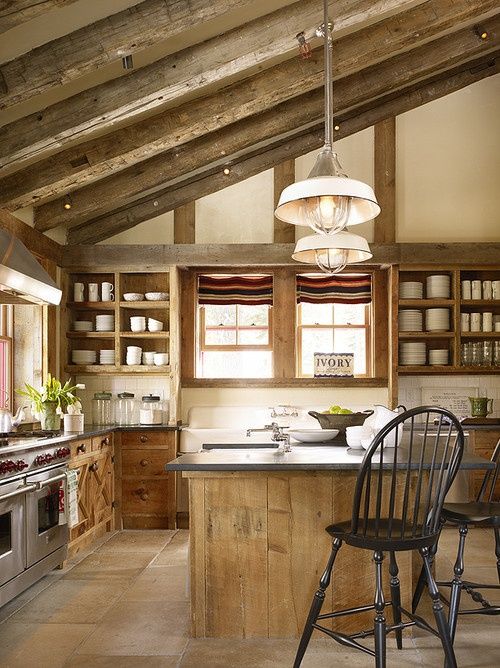 a rustic kitchen with wooden cabinetry, exposed wooden beams for more coziness, dark chairs and pendant lamps and much natural light