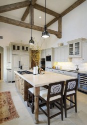 a welcoming neutral kitchen with farmhouse cabinetry, a wooden kitchen island, dark chairs and exposed wooden beams for much coziness and a warm feel