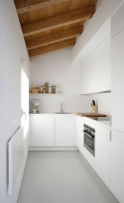 a minimalist white kitchen with sleek cabinetry, a wooden ceiling with wooden beams that softens and warms up the space and brings interest to it