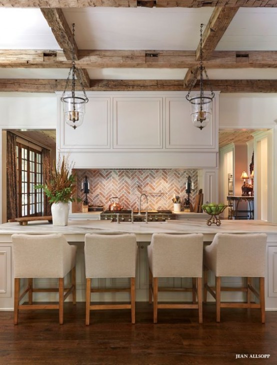 a neutral vintage kitchen with chic cabinetry, a large kitchen island, wooden beams and pendant lamps, neutral upholstered stools is very chic and cozy