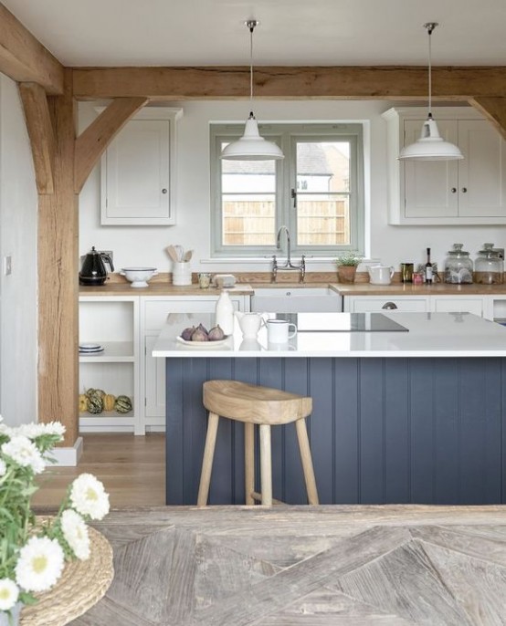 a contemporary white kitchen with wooden countertops, a navy kitchen island, wooden beams and pillars and white pendant lamps