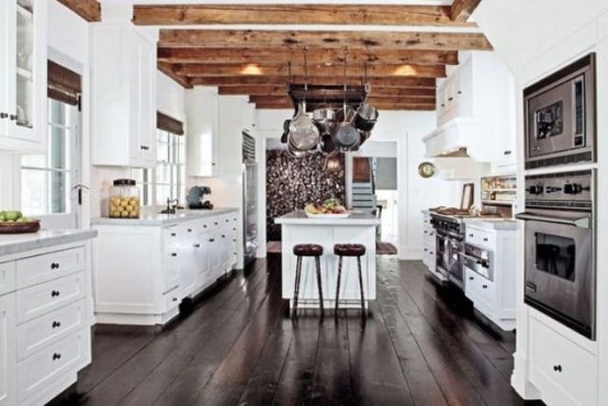 a white farmhouse kitchen with a dark wooden floor and rich tone wooden beams that add coziness, warmth and a welcoming feel